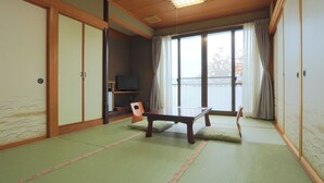 Une pièce de style japonais traditionnel, avec un sol recouvert de tatamis, une table basse, un téléviseur et des portes coulissantes.