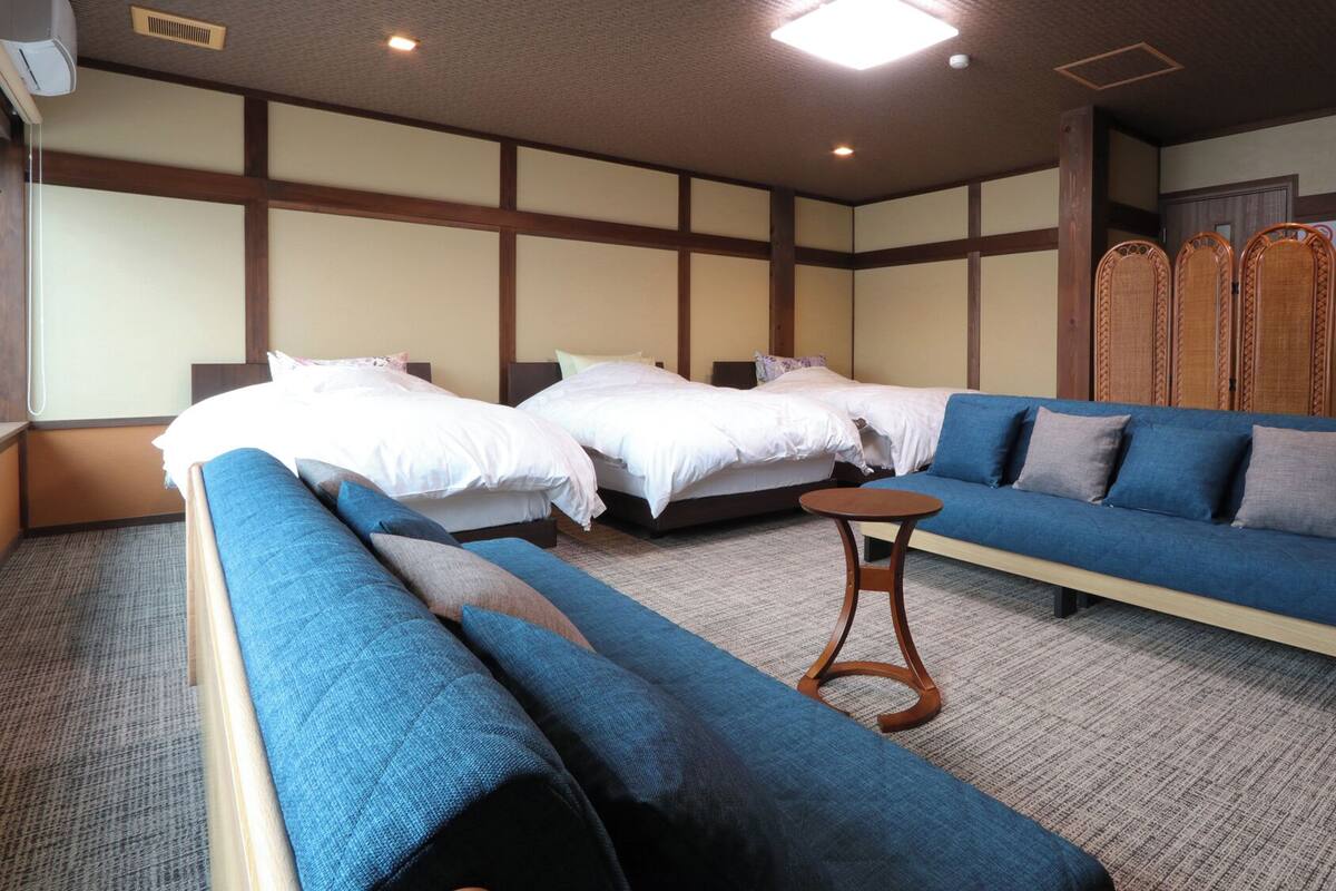A hotel room with two beds, a sofa, a small table, and traditional wooden decor.