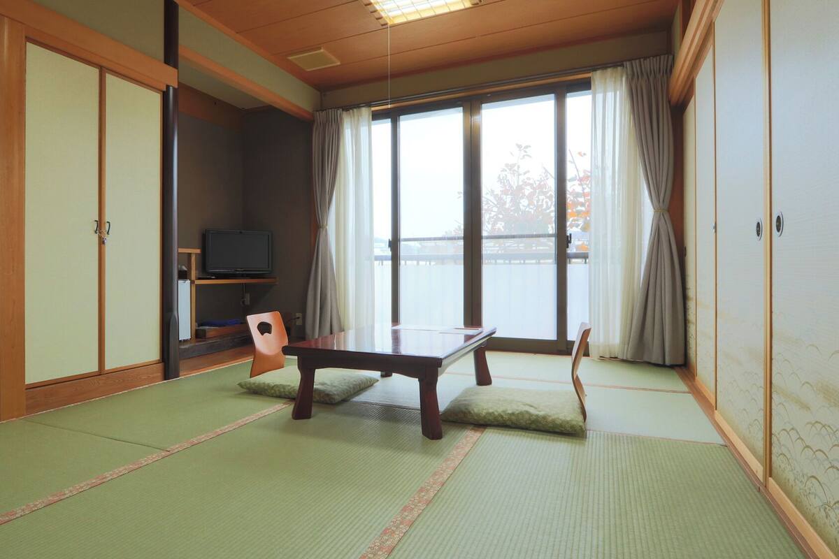 A traditional Japanese room with tatami flooring, a low table, a television, and sliding doors.