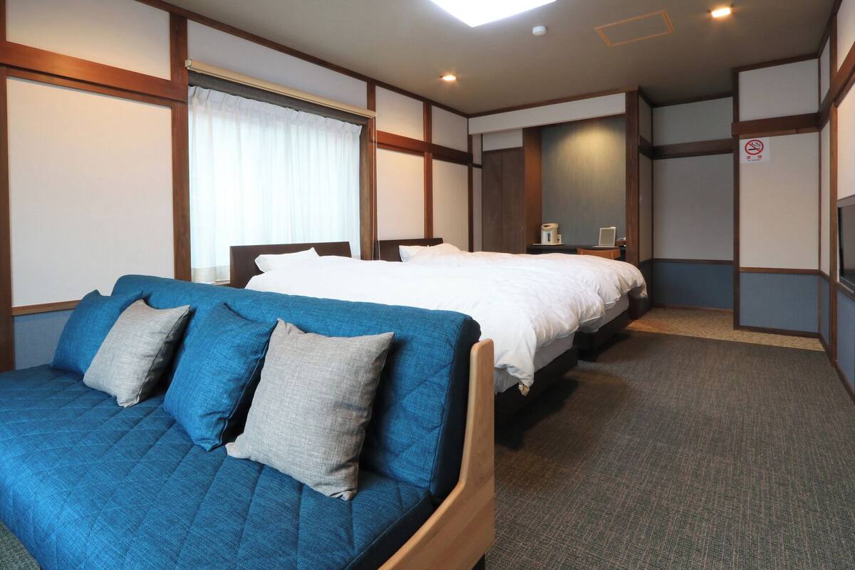 A hotel room with a blue sofa, a double bed, a television, and a window with curtains.
