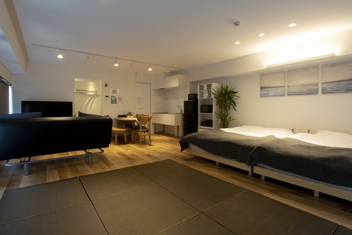 A modern hotel room with a bed, a desk, a chair, a television, and a plant.