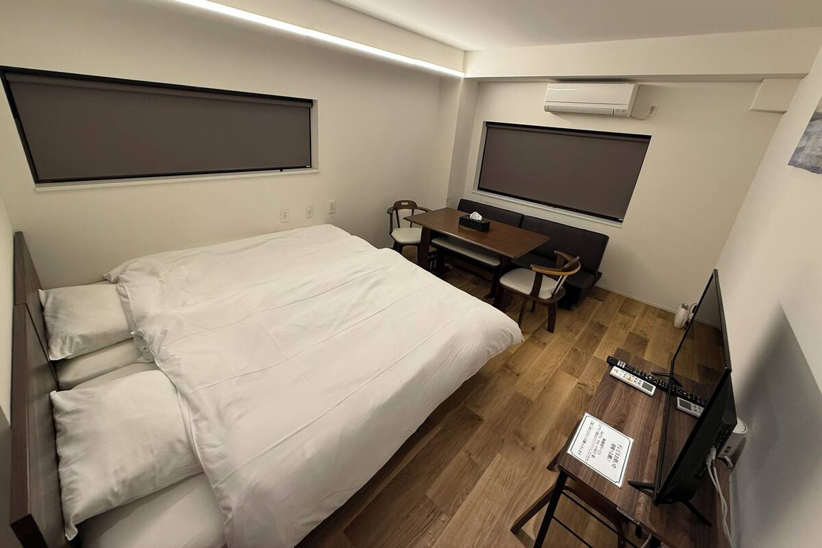 A hotel room with a bed, a desk with a computer, a TV, and an air conditioner.