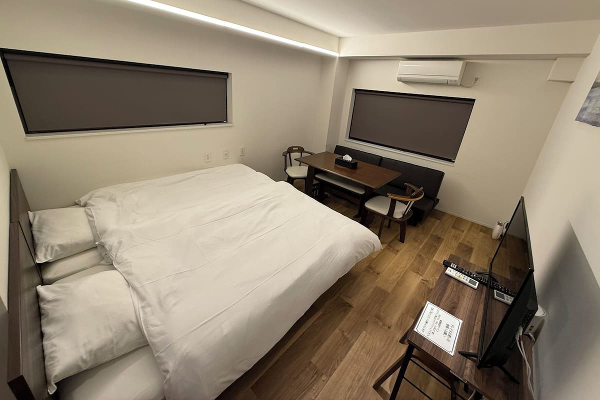 A hotel room with a bed, a desk with a computer, a TV, and an air conditioner.