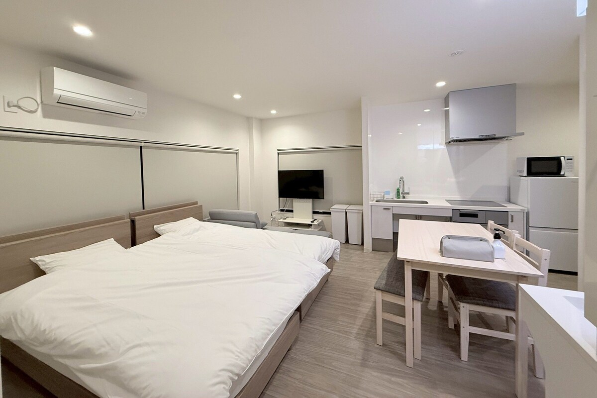 Ein modernes Hotelzimmer mit einem Bett, einem Schreibtisch mit Stuhl, einem Fernseher, einer Küchenzeile und einer Klimaanlage.
