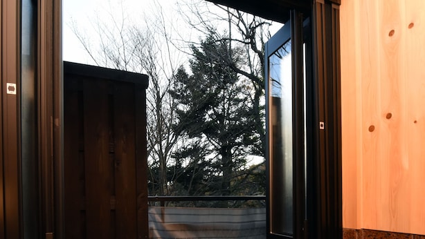 A bathroom with a bathtub, a wooden door, and a view of trees outside. - Mitaniya (Ito)
