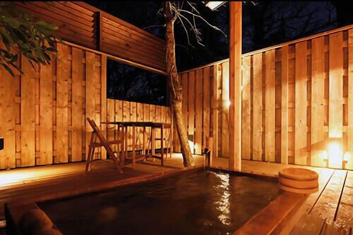 Une terrasse en bois avec un jacuzzi, une table et des chaises.