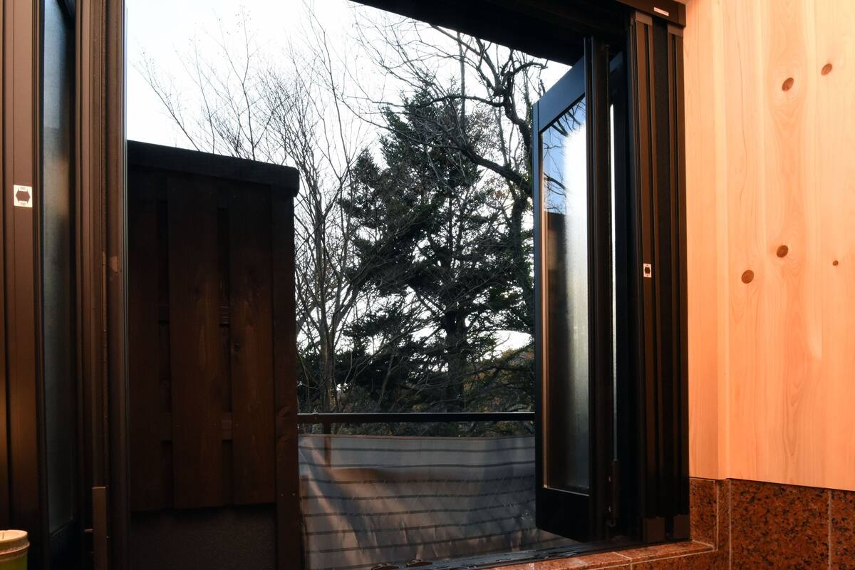 Une salle de bain avec une baignoire, une porte en bois et une vue sur les arbres à l’extérieur.