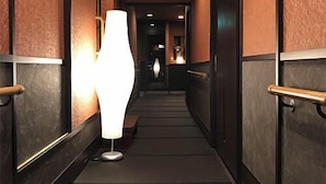 A hallway with a textured wall, a floor lamp, and a door with a handle. - Mitaniya (Ito)