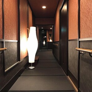 A hallway with a textured wall, a floor lamp, and a door with a handle. - Mitaniya (Ito)
