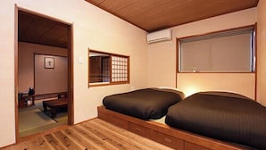 A room with a wooden floor, a bed with a dark mattress, a small window with a grid pattern, and a wall-mounted air conditioner. - Mitaniya (Ito)