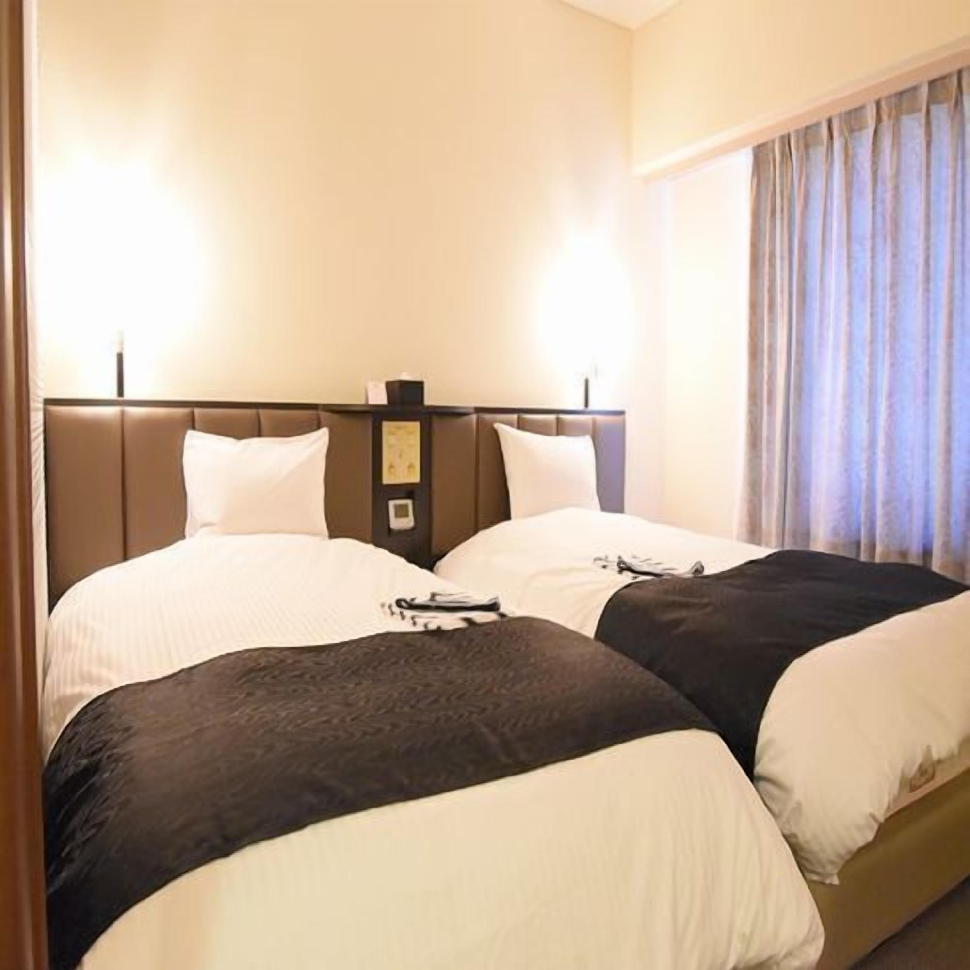 Quarto de hotel com duas camas, uma mesa de cabeceira e uma janela com cortinas.