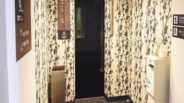 Un couloir étroit aux murs recouverts d’un papier peint à motifs, un comptoir d’accueil et des panneaux indicateurs.