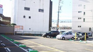 Un parking avec des places délimitées, un panneau indicateur et des bâtiments en arrière-plan.