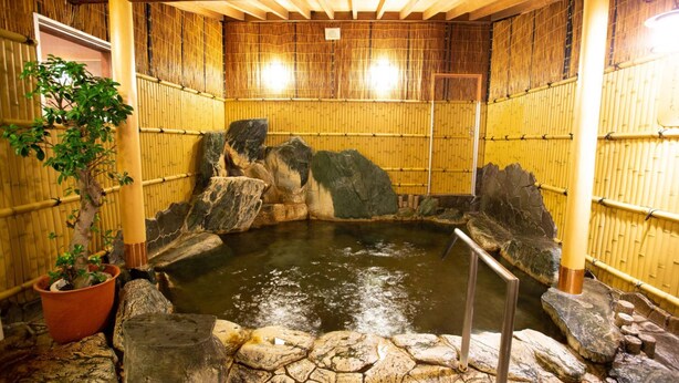A traditional Japanese onsen with a rock bath, bamboo walls, and a potted plant. - Yurara Kazoku No Yu (Matsuyama)