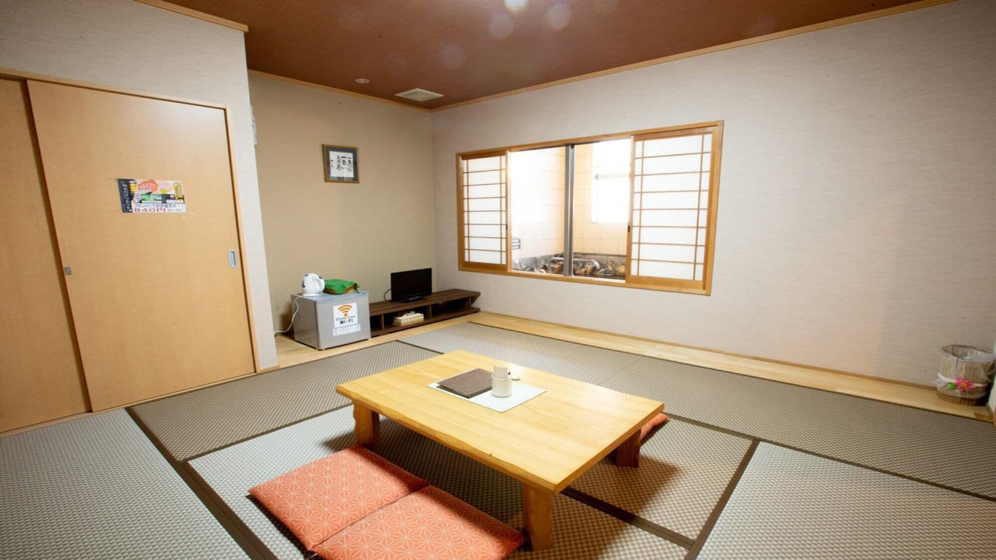 A traditional Japanese room with tatami flooring, a low wooden table, a TV, and a sliding door.