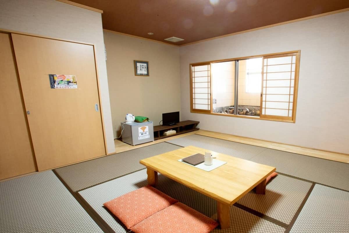 Ein traditioneller japanischer Raum mit Tatami-Böden, einem niedrigen Holztisch, einem Fernseher und einer Schiebetür.
