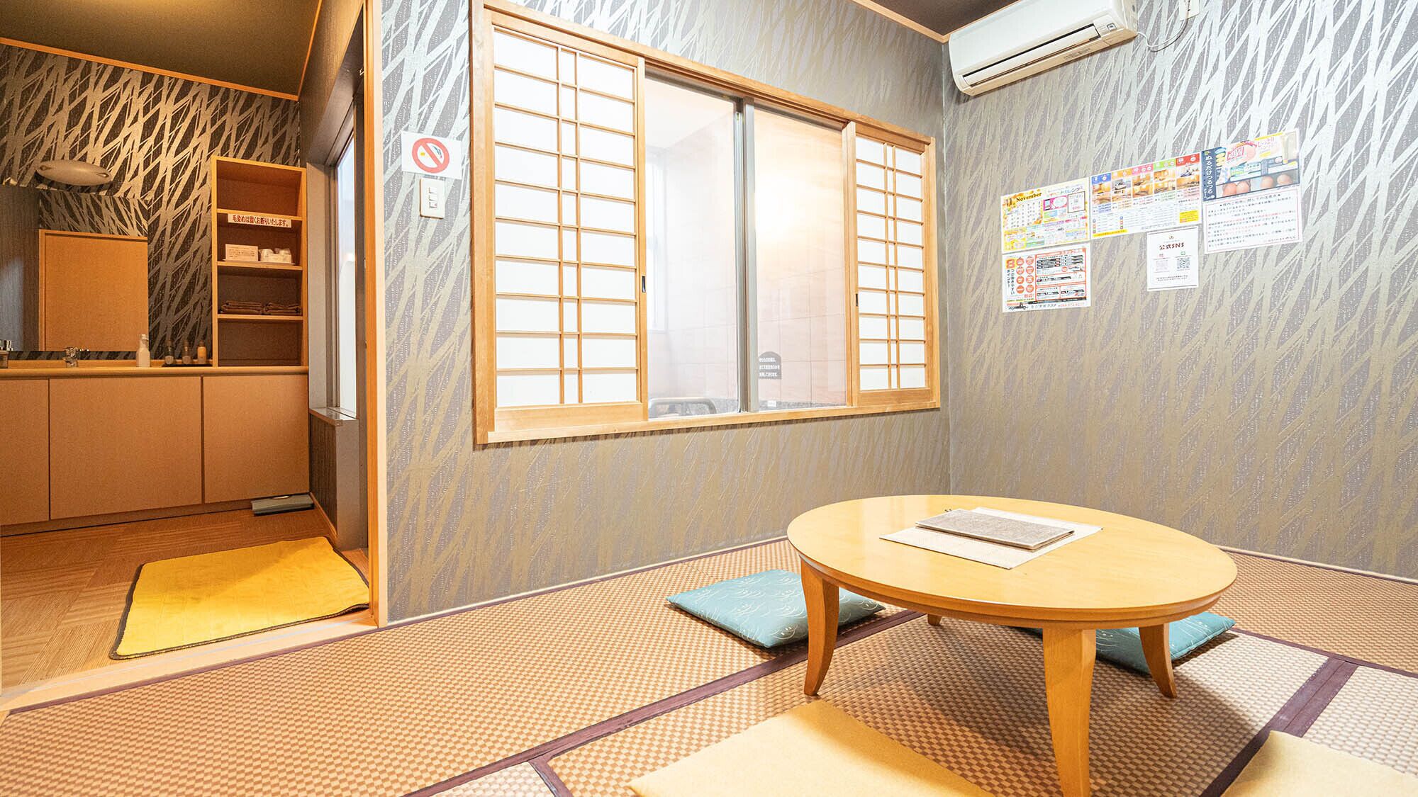 Una habitación japonesa tradicional con suelo de tatami, un biombio shoji, una mesa redonda y una estantería con objetos.