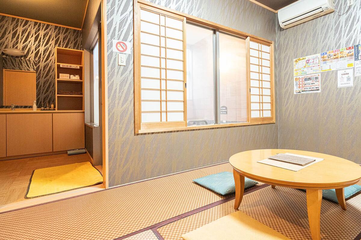 Ein traditioneller japanischer Raum mit Tatami-Boden, Shoji-Schirm, einem runden Tisch und einem Regal mit Gegenständen.