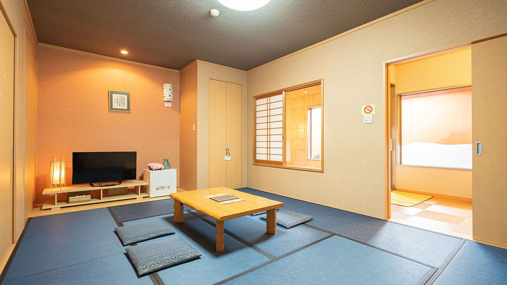 Una habitación tradicional japonesa con suelo de tatami, una televisión, una mesita y puertas correderas.
