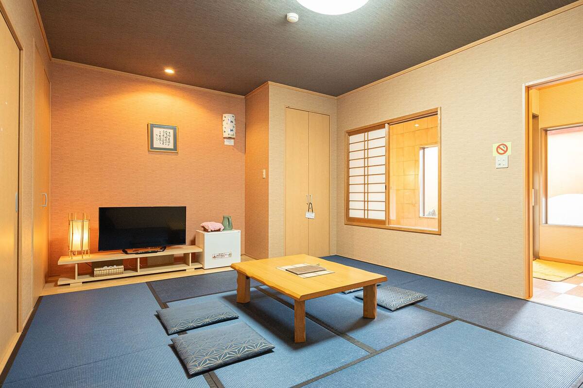 Ein traditioneller japanischer Raum mit Tatami-Böden, einem Fernseher, einem kleinen Tisch und Schiebetüren.