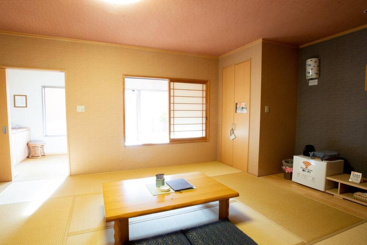 Ein traditioneller japanischer Raum mit Tatami-Boden, einem niedrigen Holztisch, einer Schiebetür und einem Fernseher auf einem Standfuß.