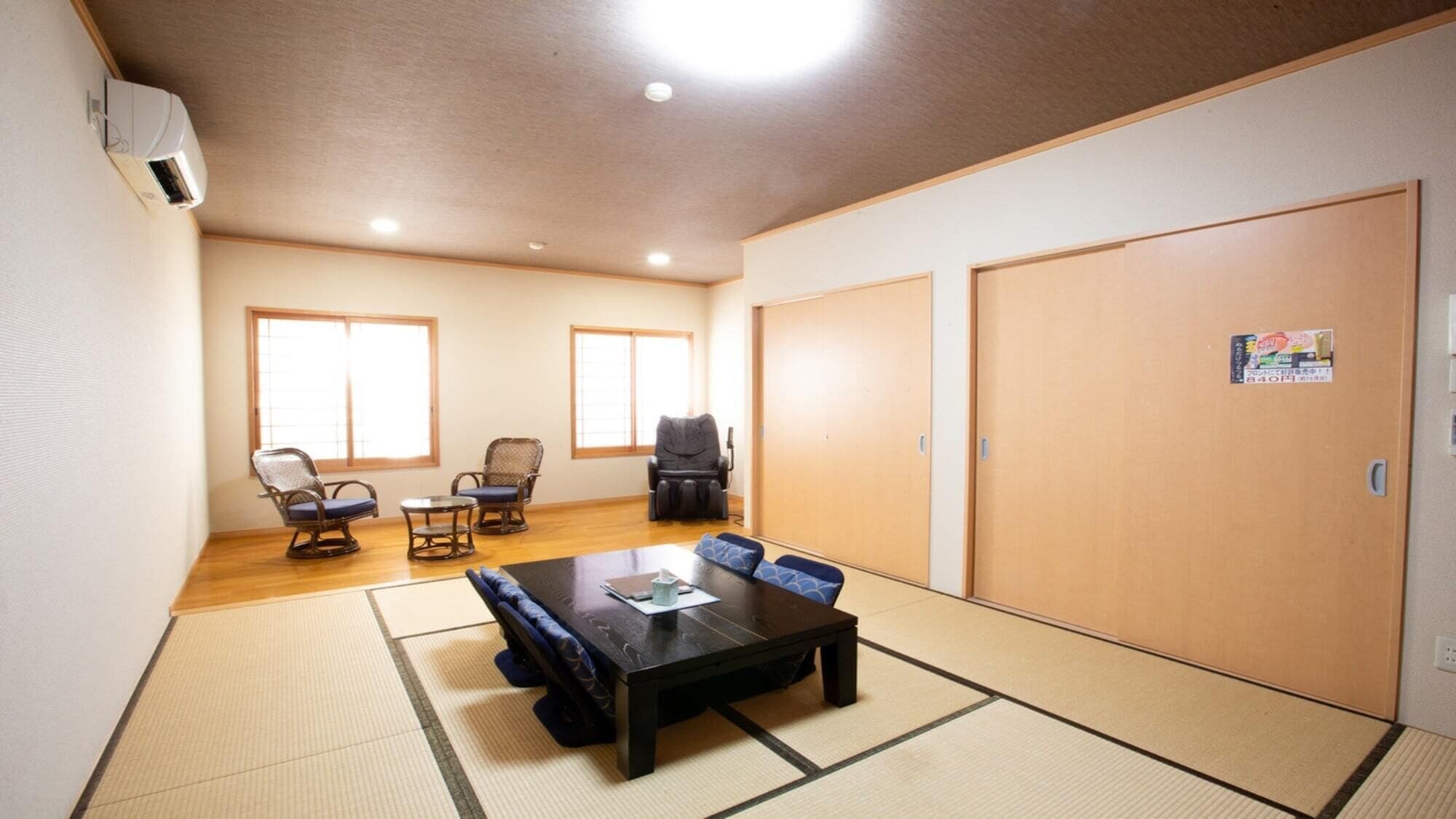 A room with tatami flooring, a tatami mat table, two tatami mats, a massage chair, two chairs, and a large sliding door.