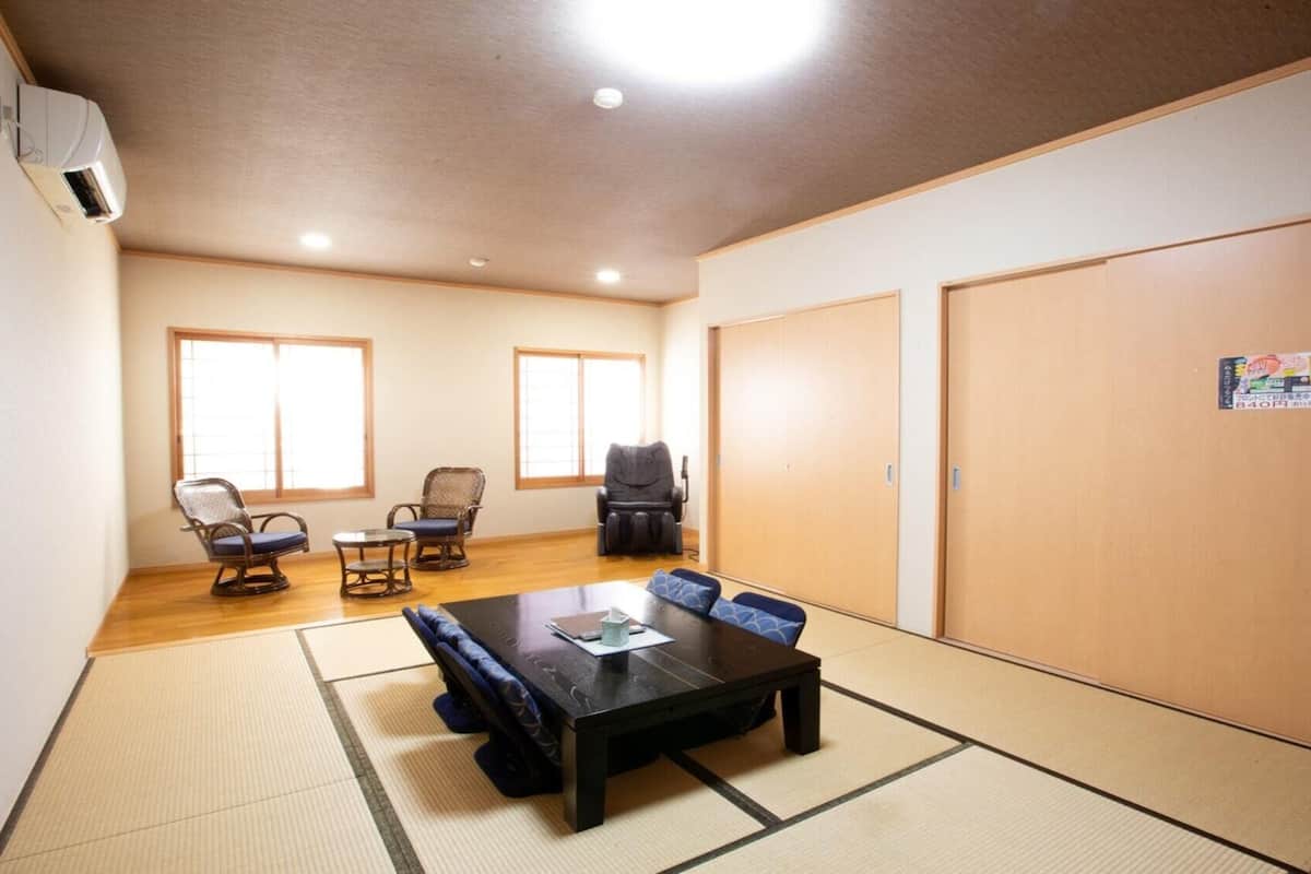 Ein Zimmer mit Tatami-Boden, einem Tatami-Tisch, zwei Tatami-Matten, einem Massagesessel, zwei Stühlen und einer großen Schiebetür.