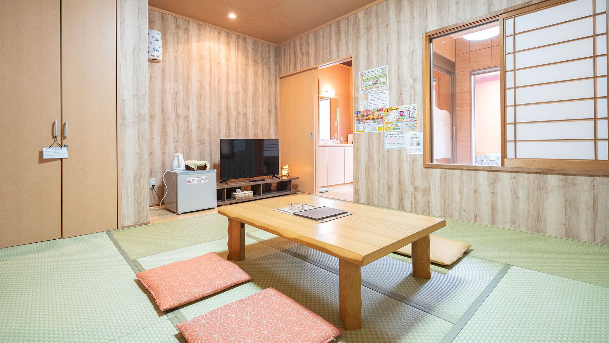 Una habitación japonesa tradicional con suelo de tatami, una mesa de madera baja, un televisor y una pequeña kitchenette.