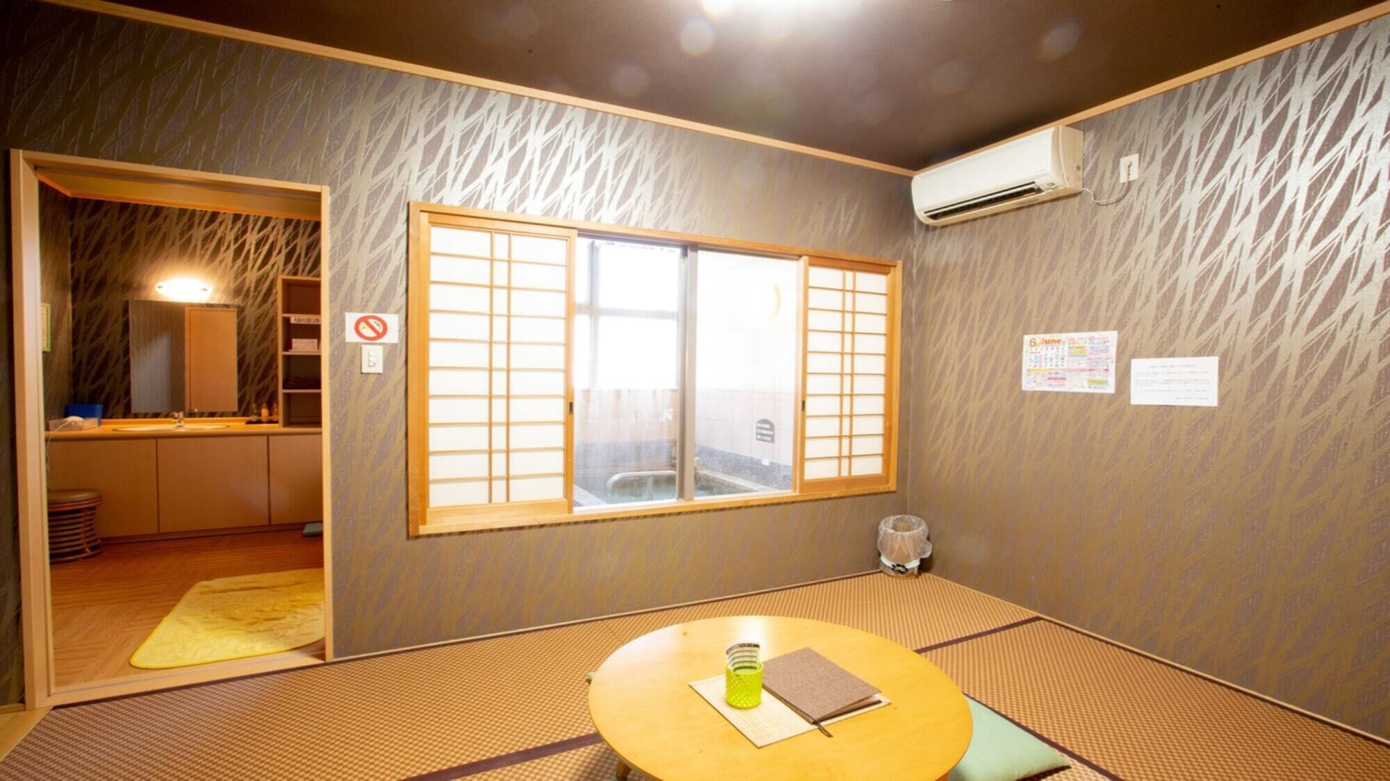 A traditional Japanese room with tatami flooring, a shoji screen window, a small table with a green container and a notebook, and a wall-mounted air conditioner.