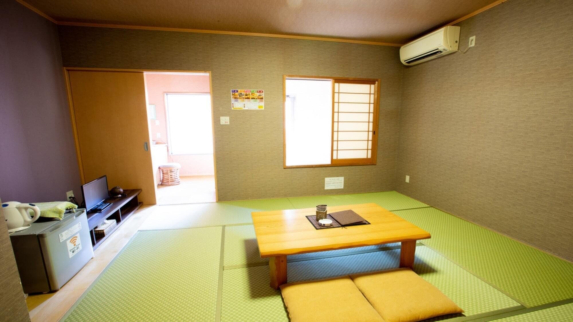 A room with tatami flooring, a wooden table, a sofa, a desk with a computer, and an air conditioning unit.