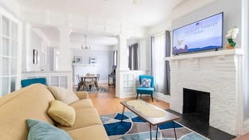 En rummelig stue med en beige sofa, en pejs og et tv ophængt over den.