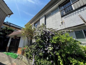 A residential building with a tiled roof, a front door, and a small garden with flowering plants. - Aizawaso (Kawazu)