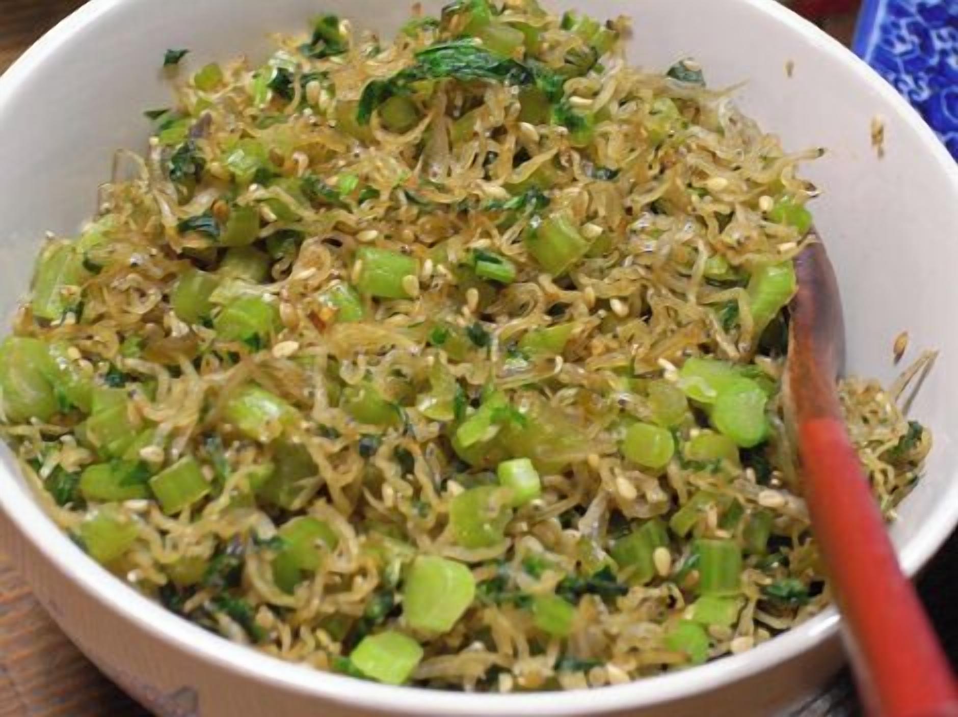 A bowl of stir-fried noodles with green vegetables.