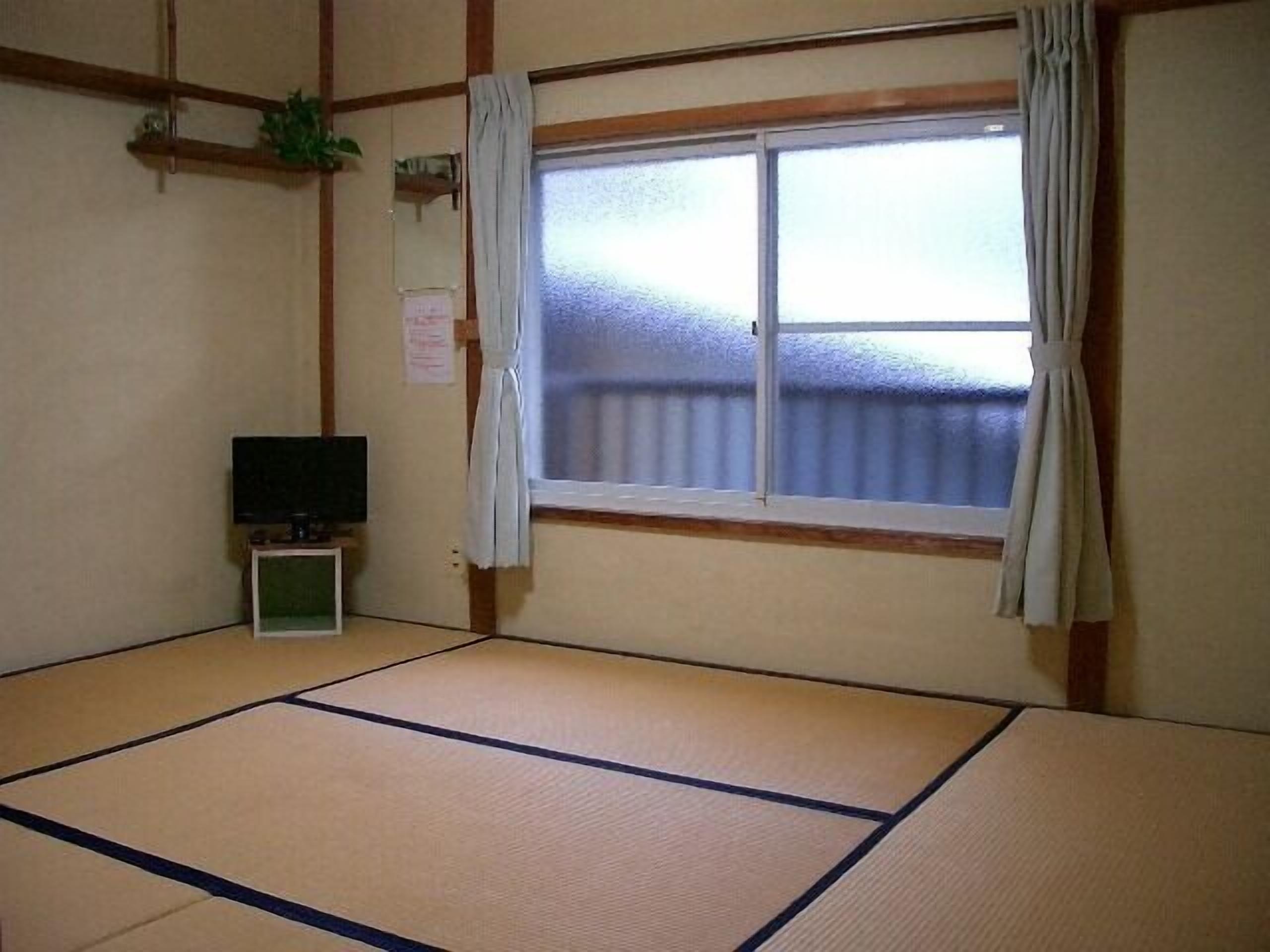 Habitació amb tatami, televisió, finestra amb cortines i una petita estant amb una planta.