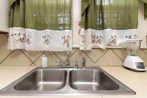 Una cucina con un lavello in acciaio inossidabile a due vasche, un frullatore bianco e una bottiglia di sapone per le mani.
