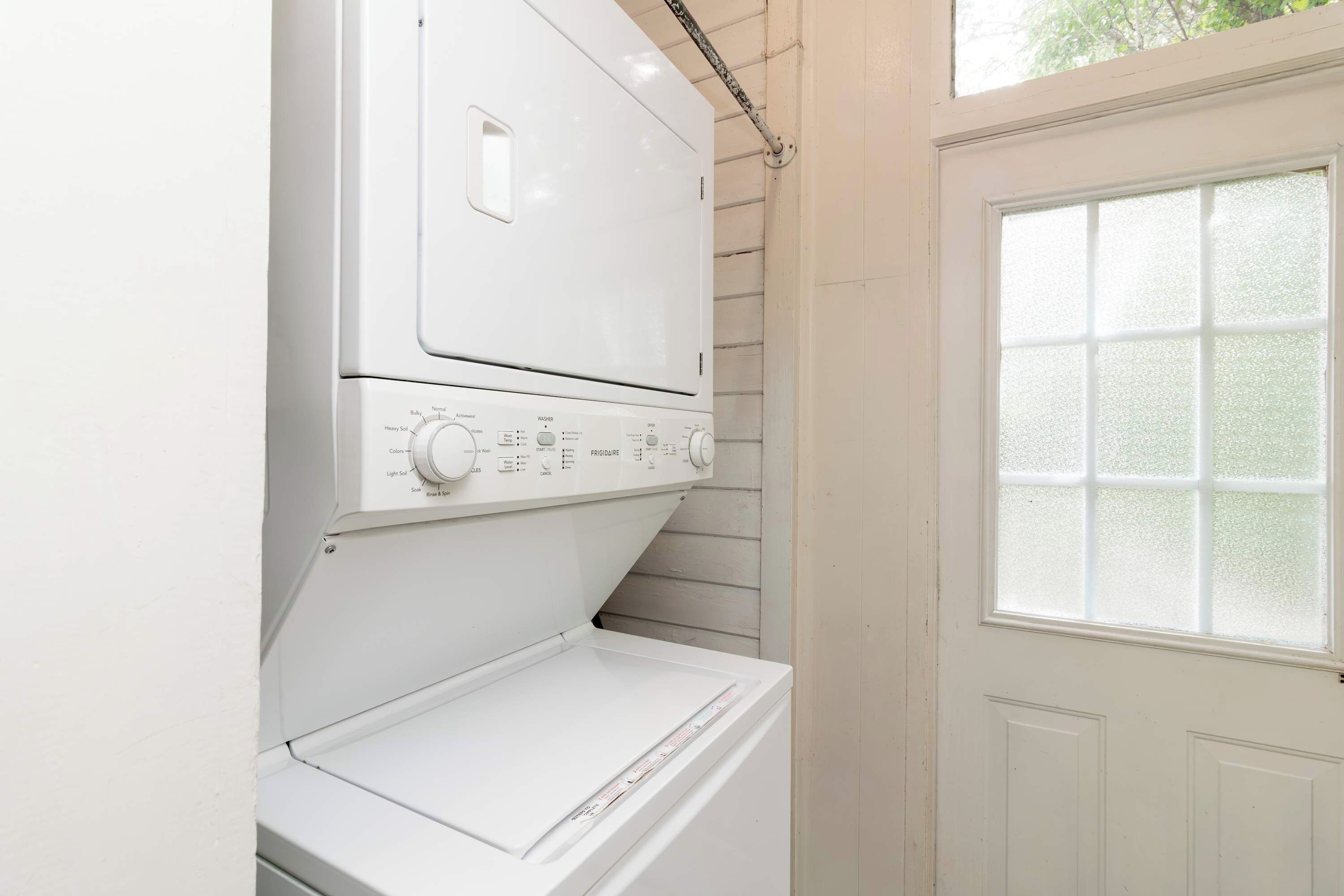 A white front-loading washer and dryer unit with a control panel, installed against a wall with a window above.