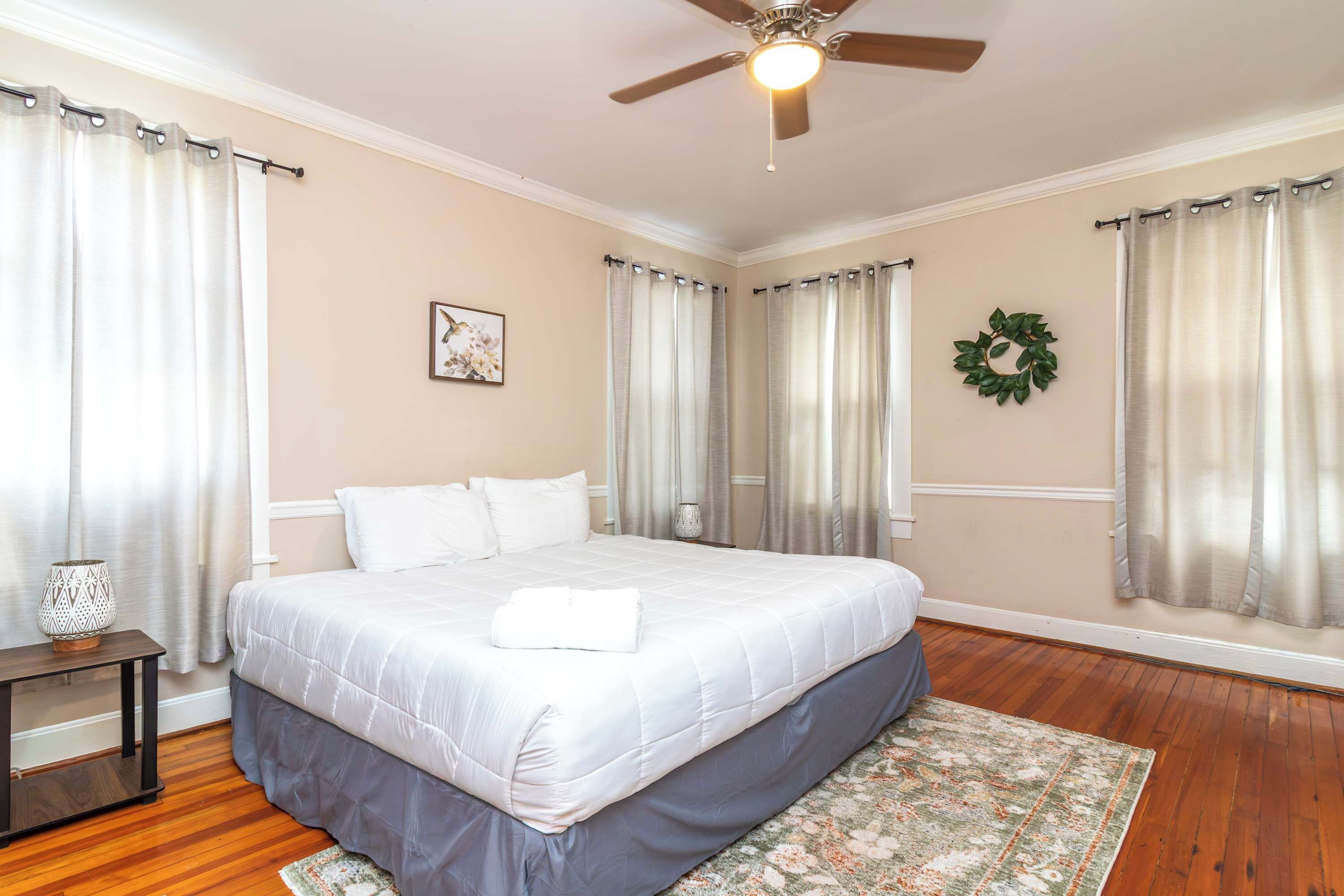 Ein Schlafzimmer mit Bett, Deckenventilator, Wandleuchte, gerahmtem Bild und einem Wandkranz.