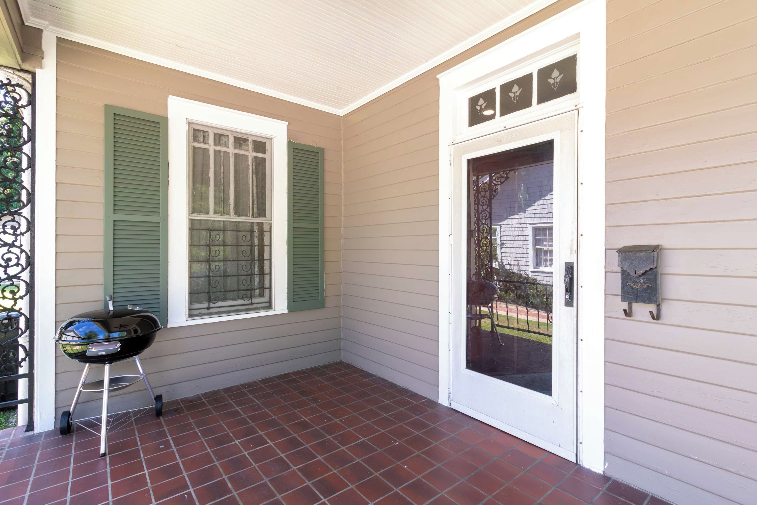Eine überdachte Veranda mit Grill, eine Tür mit Fenster und ein Fliesenboden.