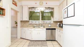 A compact kitchen with white cabinets, a built-in dishwasher, a microwave, and a window with floral curtains.