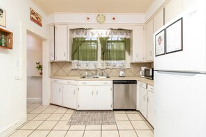 Una cucina compatta con mobili bianchi, lavastoviglie integrata, forno a microonde e una finestra con tende floreali.