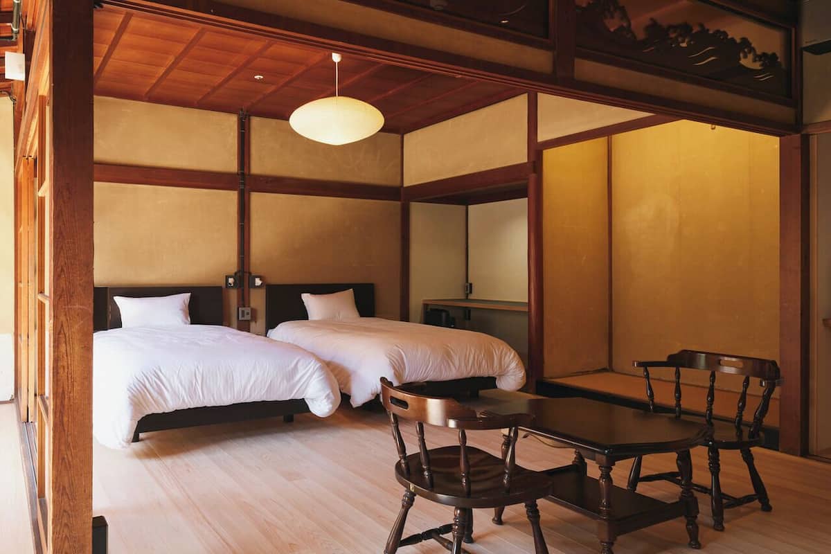 A traditional Japanese-style room with two beds, a wooden table, and chairs.