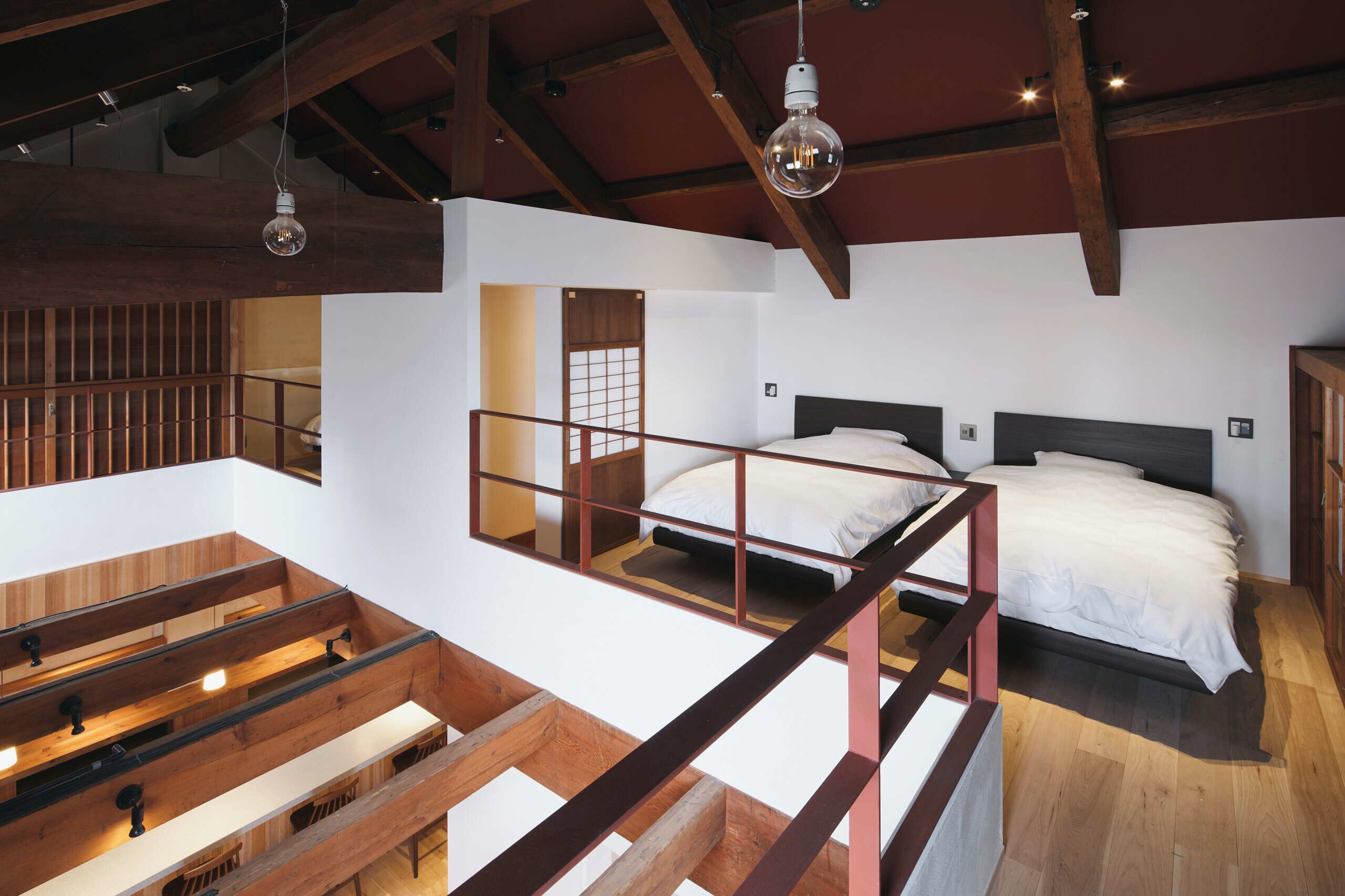 Une chambre de style loft avec un plafond haut, des poutres apparentes, un lit superposé et une mezzanine aménagée en coin salon.