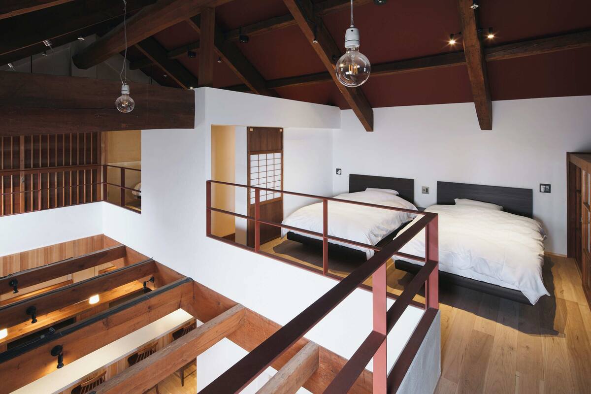 A loft-style bedroom with a high ceiling, exposed wooden beams, a bunk bed, and a mezzanine with seating.