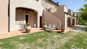 Un bâtiment orné d’arches en pierre, un patio avec un banc et des plantes en pot.