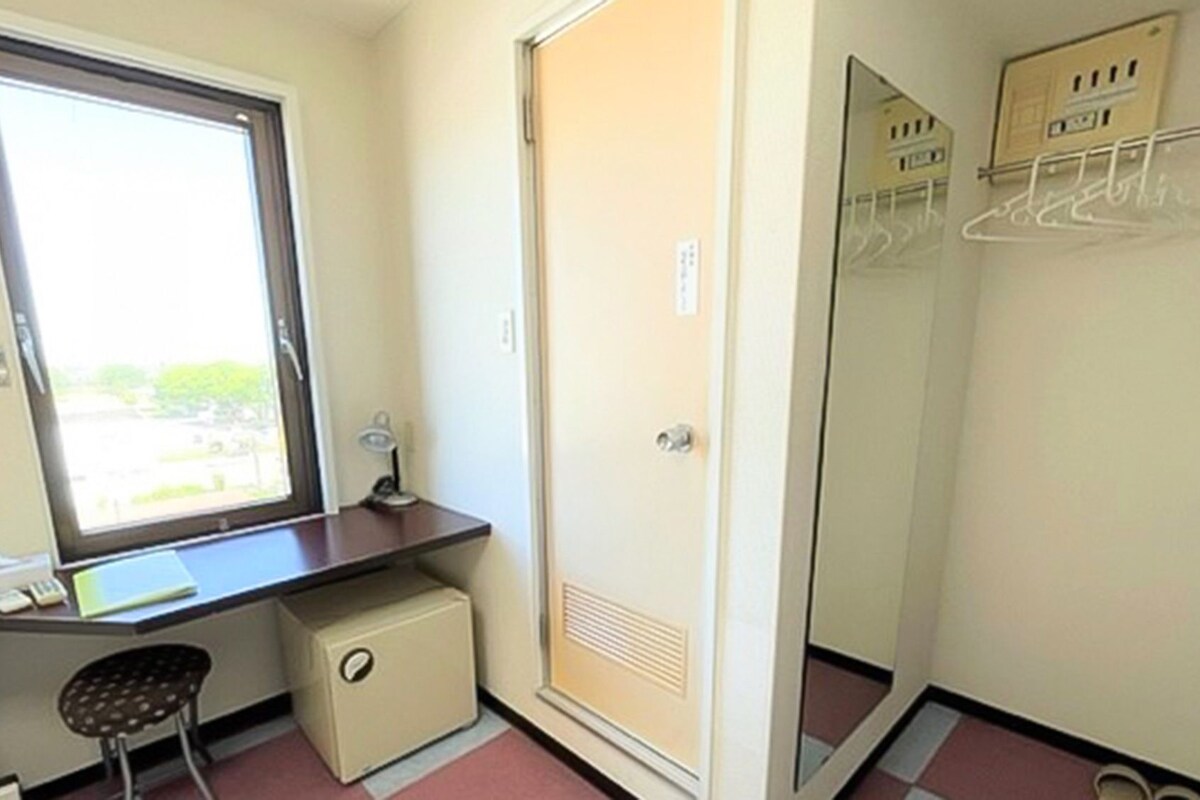 Une petite pièce comprenant un bureau, une chaise et une armoire avec un miroir.