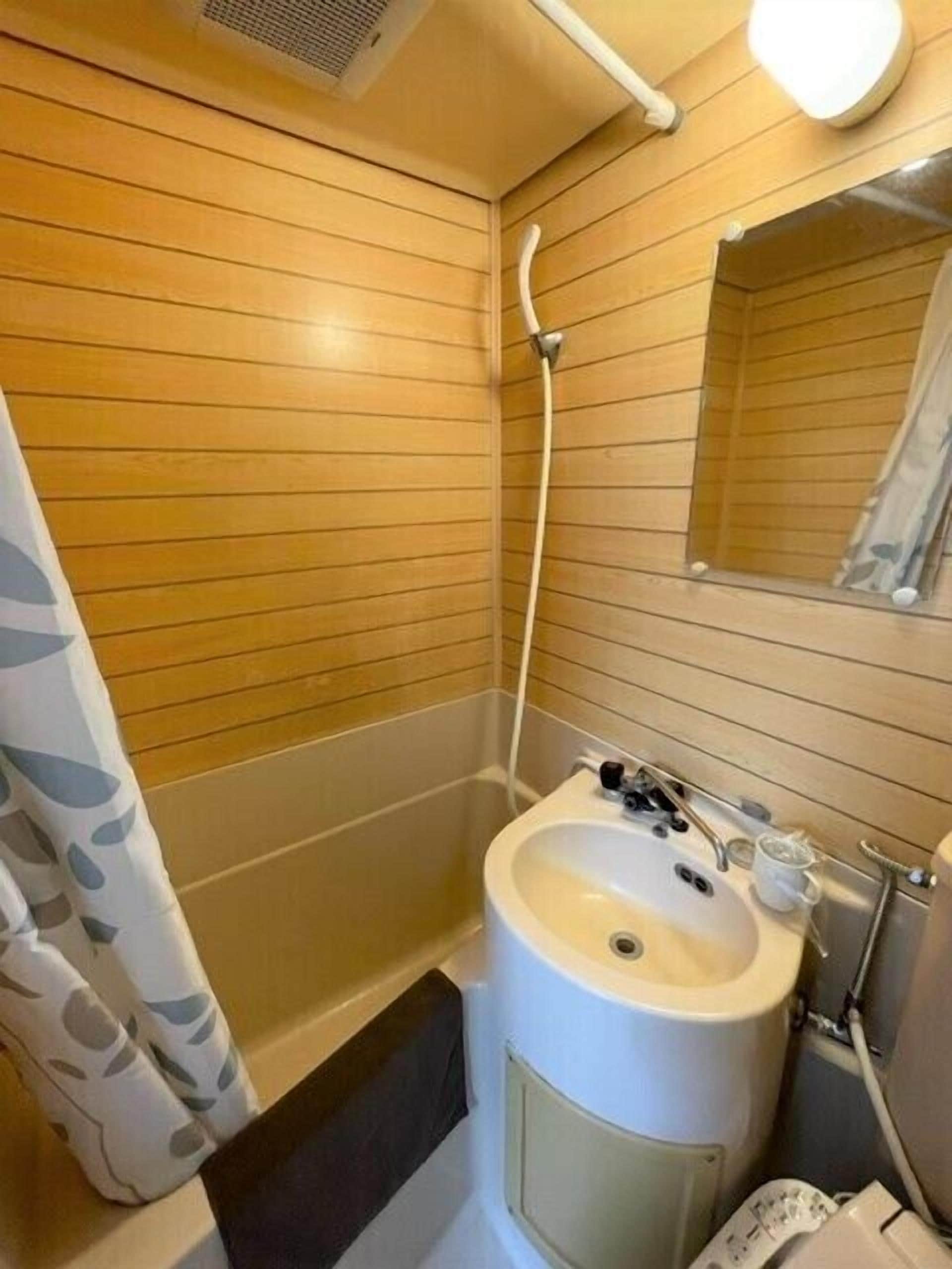 A bathroom with wooden paneling, a sink, a mirror, and a shower.