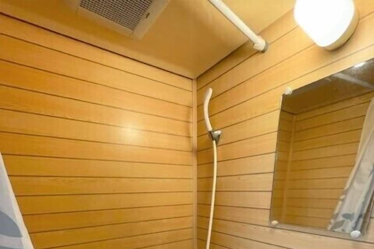 A bathroom with wooden paneling, a sink, a mirror, and a shower.