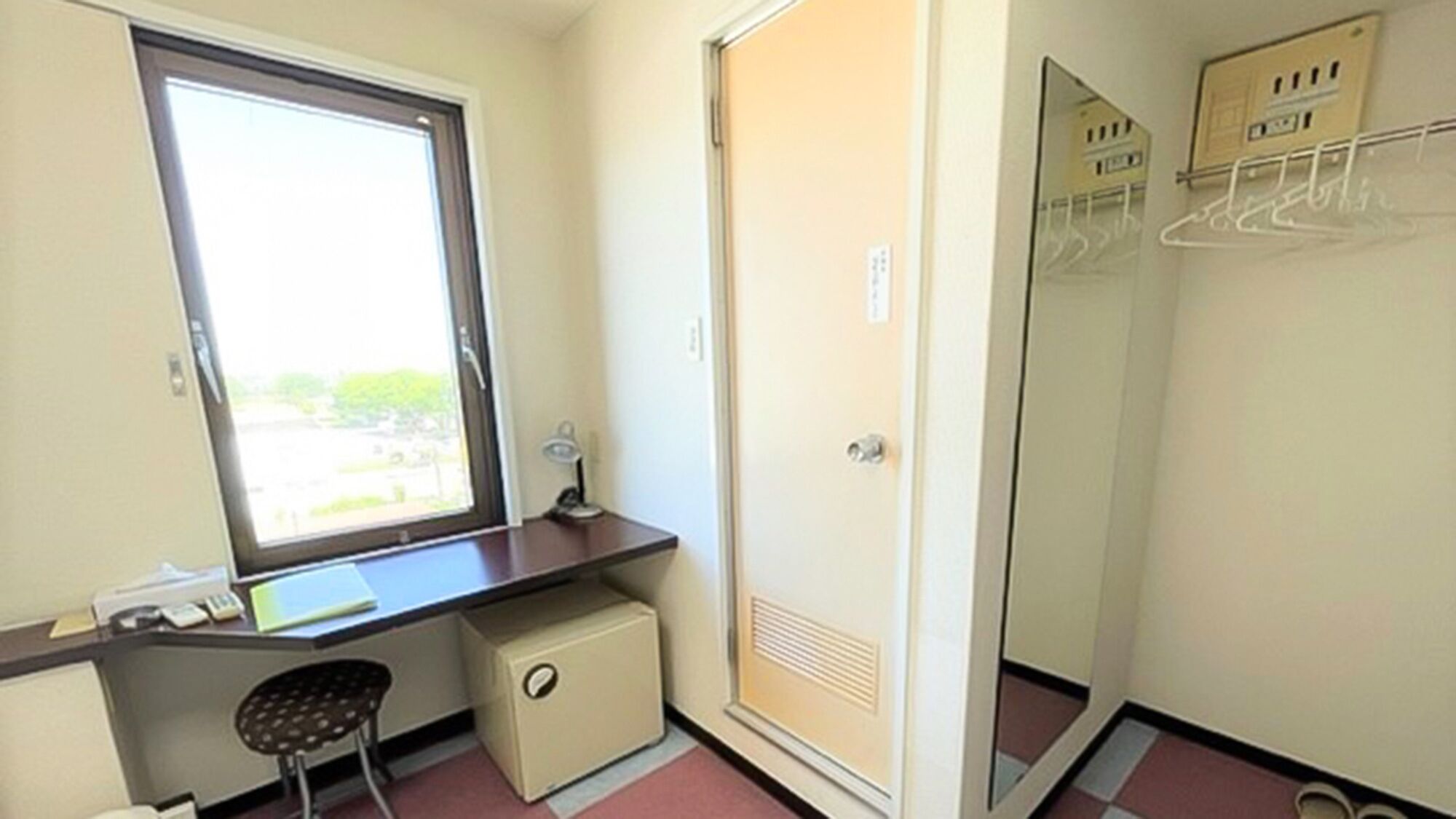 A small room with a desk, chair, and a wardrobe with a mirror.