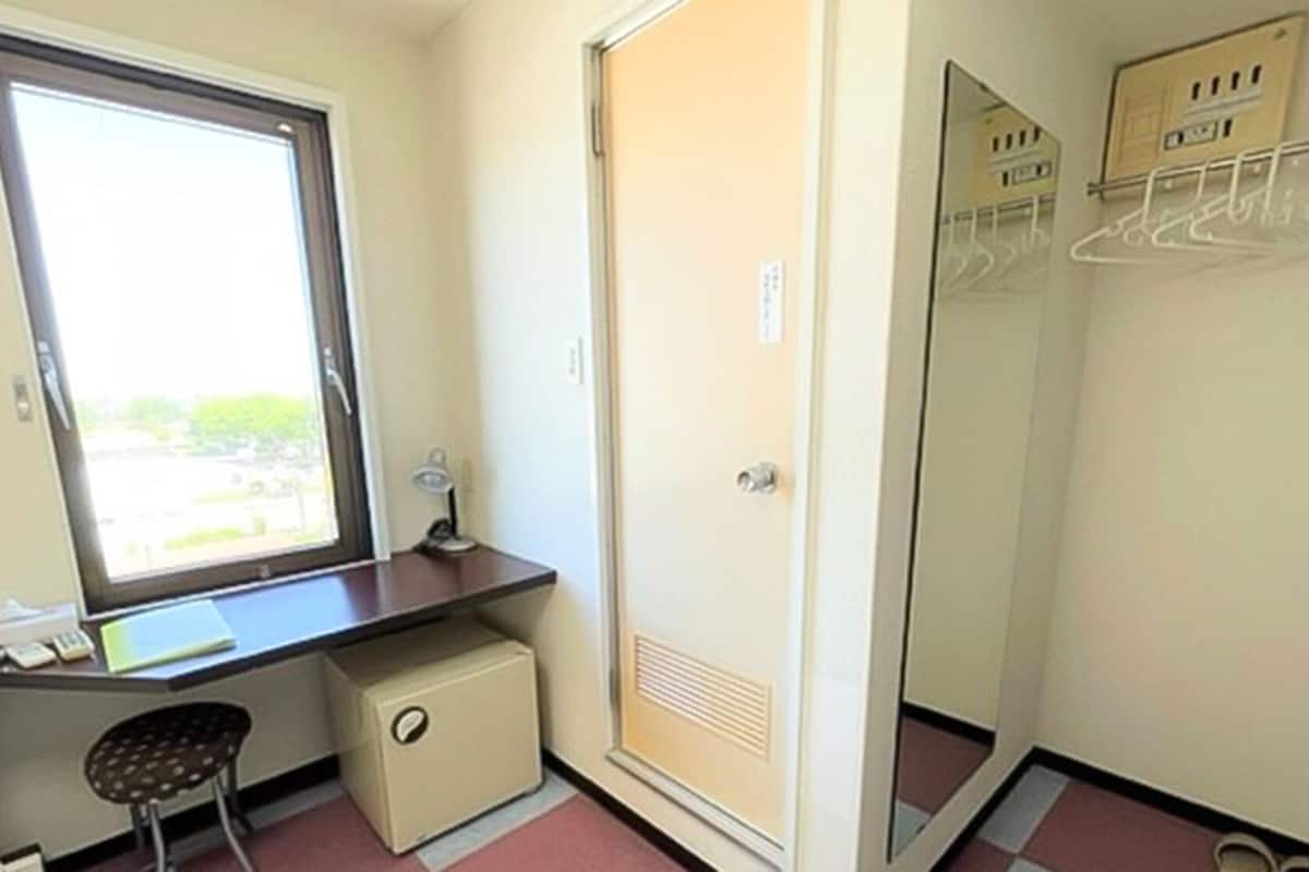 A small room with a desk, chair, and a wardrobe with a mirror.