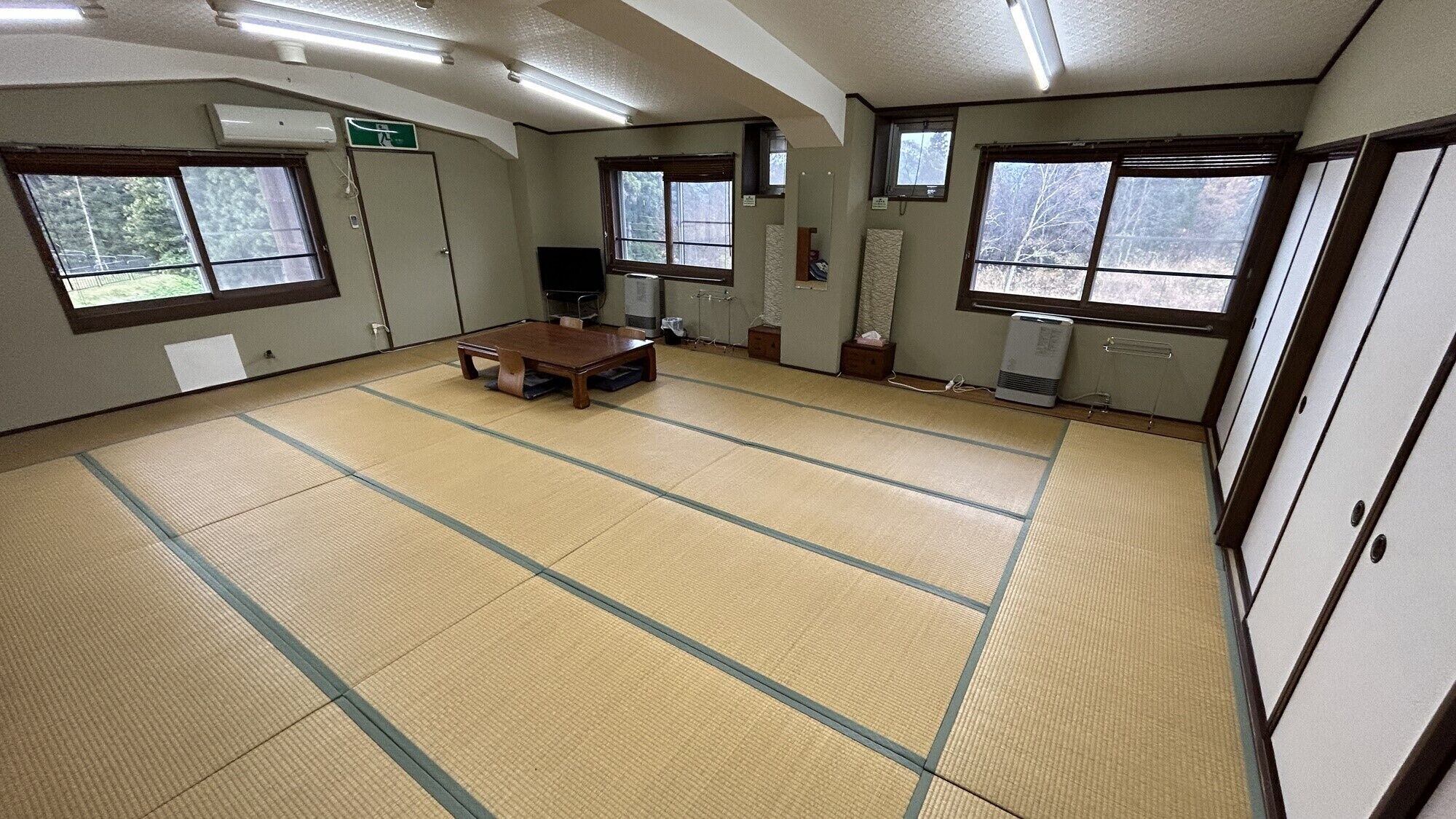 Una habitación con tatamis, una mesa de madera, ventanas y un radiador.